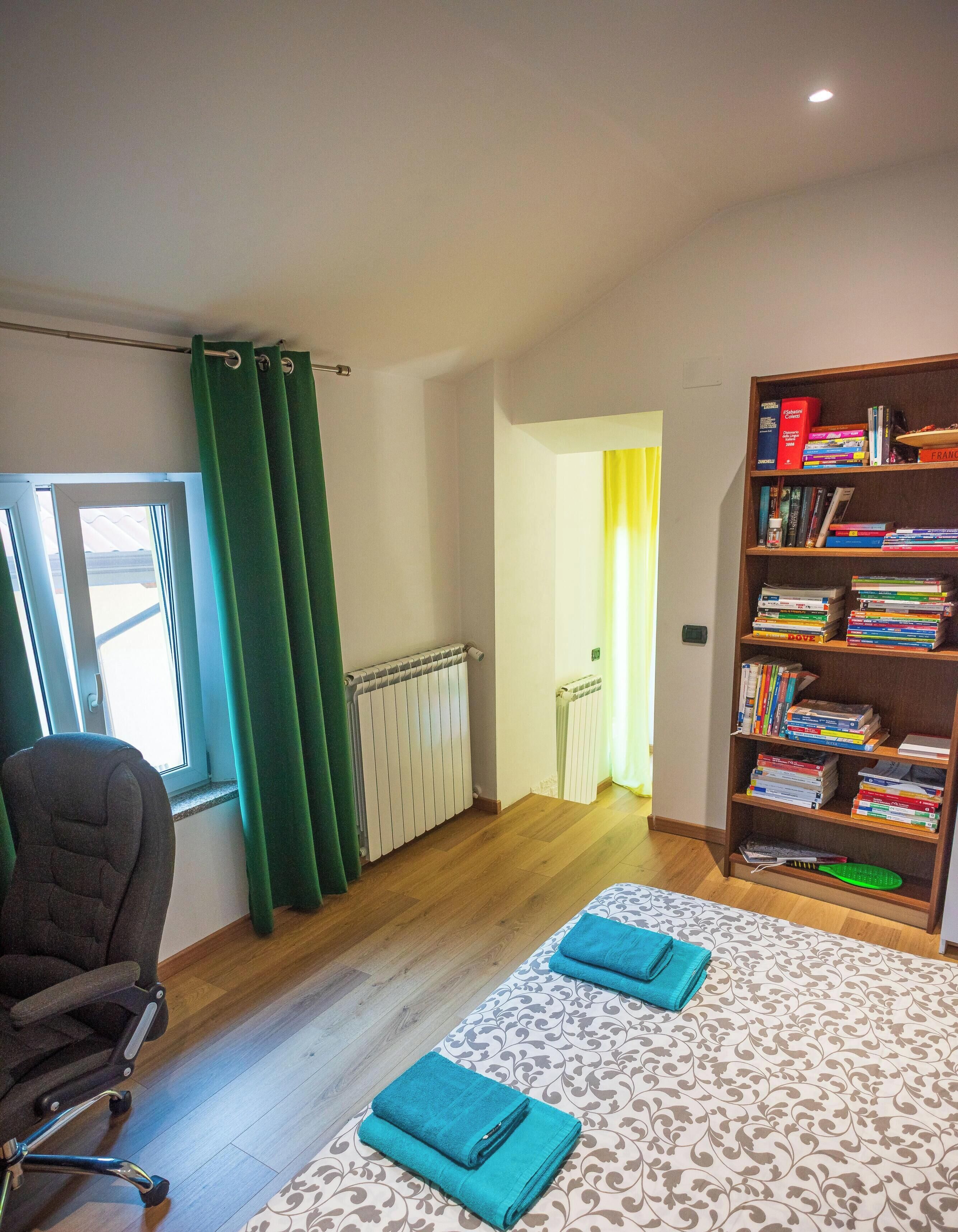 Een kamer met een radiator, een boekenkast, een stoel en een bed met opgevouwen handdoeken.