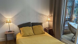 A bed with a yellow bedspread, two bedside lamps, a small rug, and a window with a view of a chair outside.