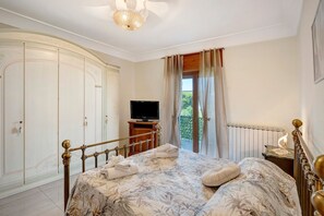 Un dormitorio con cama, televisor, armario y balcón con cortinas.