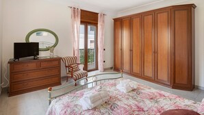 A bedroom with a bed, dresser, chair, wardrobe, and a television.