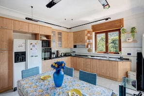 Una cocina moderna con armarios de madera, una mesa de comedor con sillas, un refrigerador y un ventanal con vista a zonas verdes.