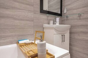 Un bagno moderno con un lavandino bianco, un vassoio di legno e un dispenser per sapone.