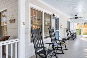 A covered porch with white siding, black rocking chairs, and a ceiling fan.