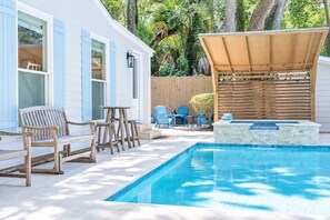A backyard with a swimming pool, wooden deck, outdoor furniture, and a wooden fence.