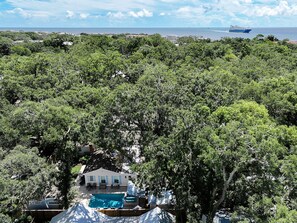 A residential area with a swimming pool, a white house, and dense greenery.