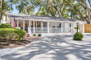 A two-story house with a porch, a flag, and a well-maintained lawn. - Porch Light Cottage - Historic District Walk to the Beach, Private Pool, Spa, Fire Pit & Guest House (Saint Simons Island)