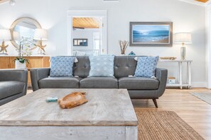 A modern living room with a grey sofa, a wooden coffee table, and a view of the ocean through a window.