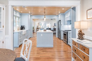 A spacious kitchen with wooden flooring, light blue cabinetry, and a central island. - Porch Light Cottage - Historic District Walk to the Beach, Private Pool, Spa, Fire Pit & Guest House (Saint Simons Island)