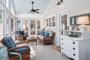 A bright, airy room with wicker furniture, a ceiling fan, and a white dresser with a 'BEACH' sign.
