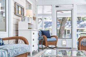 A room with wicker furniture, a white dresser, and a glass table.