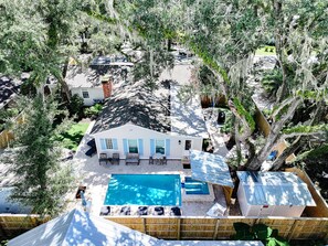 A house with a swimming pool, surrounded by trees and a fenced yard. - Porch Light Cottage - Historic District Walk to the Beach, Private Pool, Spa, Fire Pit & Guest House (Saint Simons Island)
