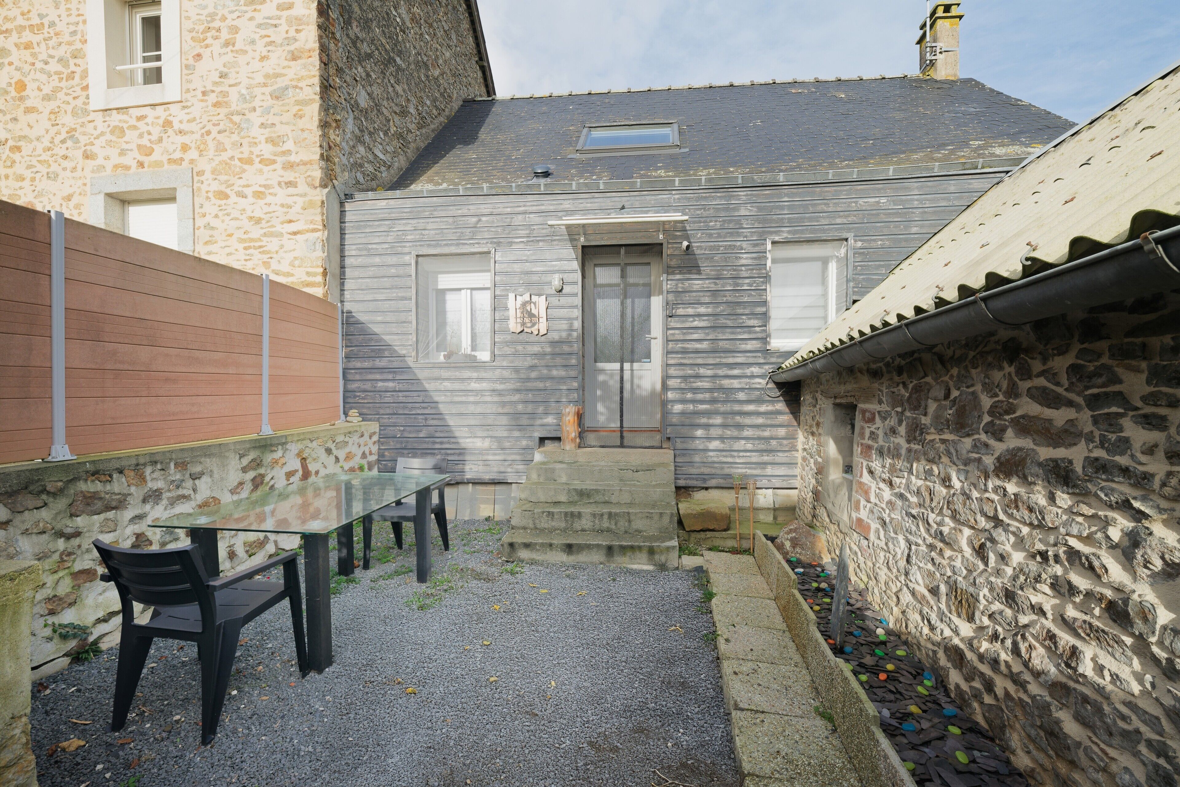 A stone building with a gravel patio, a glass table, and a black chair.