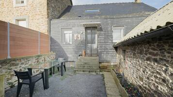 A stone building with a gravel patio, a glass table, and a black chair.