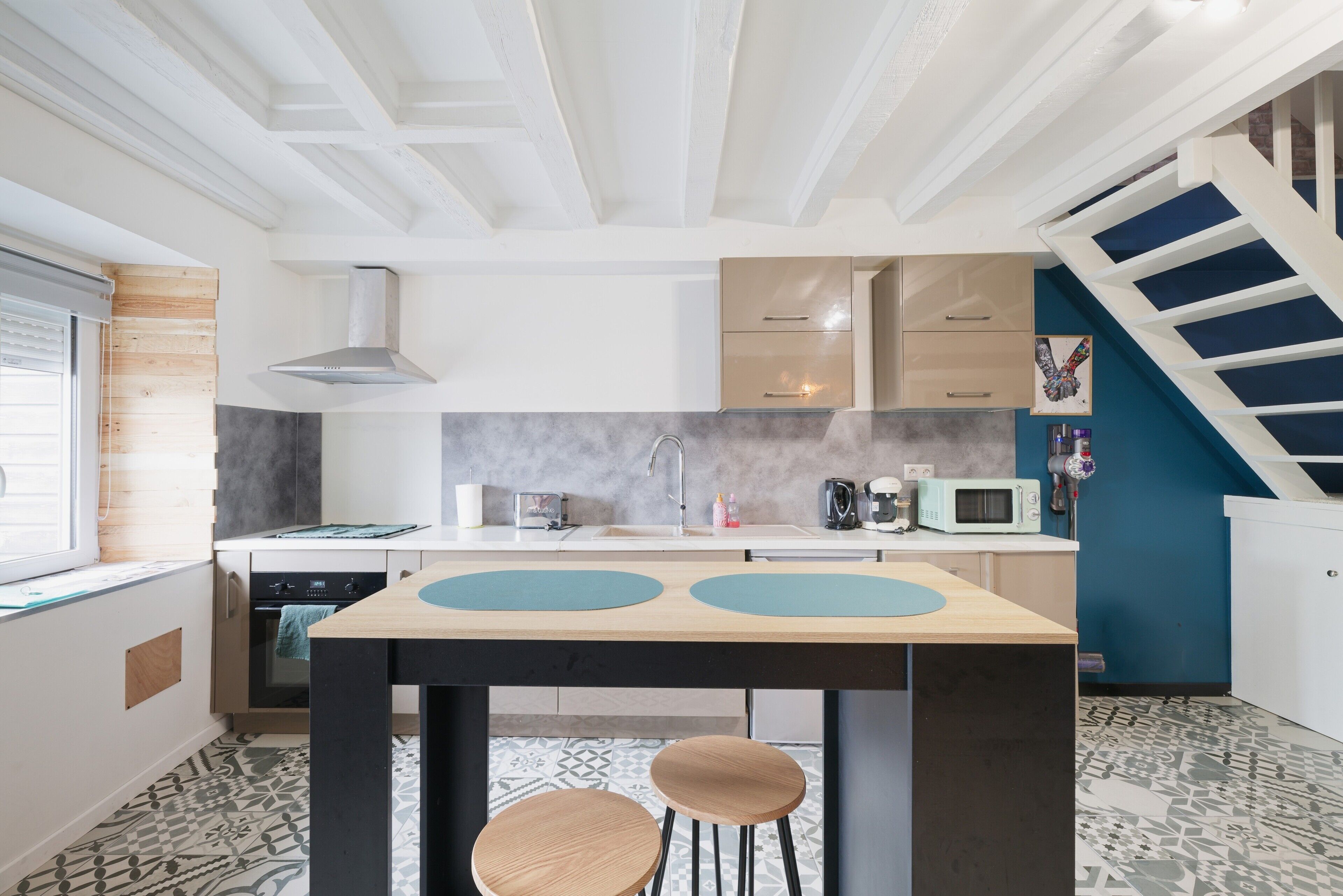 Une cuisine moderne dotée d’un îlot central, d’appareils électroménagers intégrés et d’un escalier situé sur le côté droit.