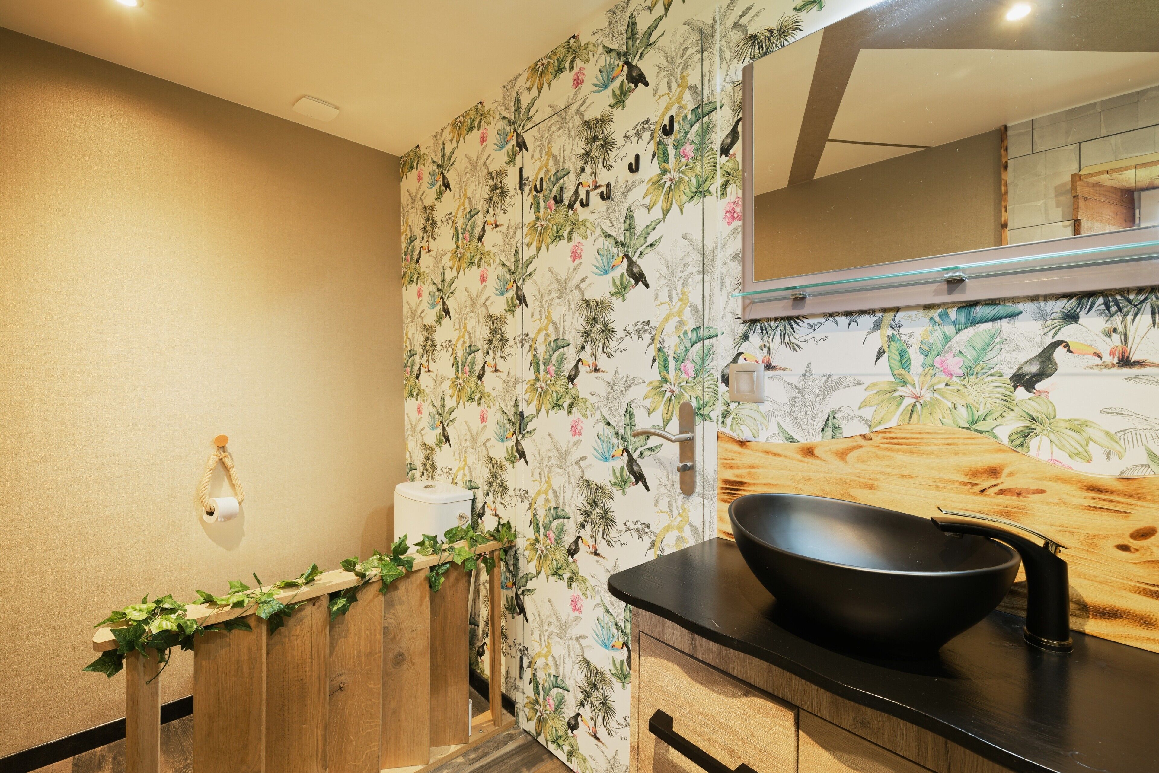 Un baño con tocador de madera, lavamanos negro y papel tapiz con motivos florales.