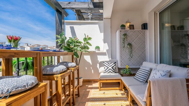 A balcony with a wooden table, chairs, a sofa, and a patterned rug.