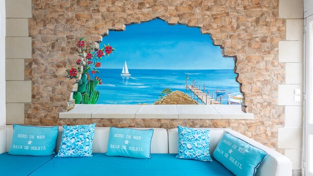 Ein Zimmer mit einer Steinwand, einem Gemälde einer Küstenszene und einem Sofa mit passenden Kissen.