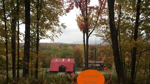 Ein rotes Bauernhaus mit einem kleinen Anbau, umgeben von Herbstlaub und Bäumen.