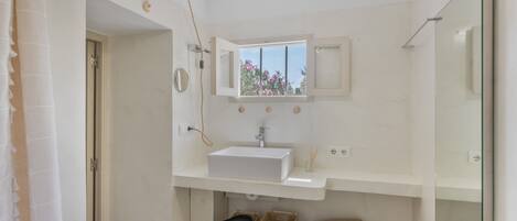 A bathroom with a white sink, a window with a view, a mirror, and a shower area.