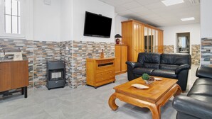 Un soggiorno con televisione, divano in pelle, mobiletto in legno e parete con decorazione effetto pietra.