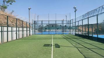 Una cancha de tenis con red, rodeada por una valla, y equipada con iluminación.