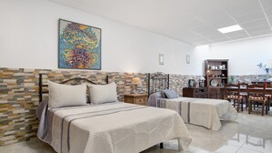 Camera d'albergo con due letti, una parete con motivo in pietra, un quadro astratto di grandi dimensioni, un mobile in legno e un'area pranzo con sedie e tavolo.