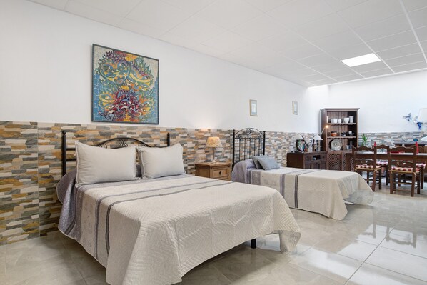 A hotel room with two beds, a stone-patterned wall, a large abstract painting, a wooden cabinet, and a dining area with chairs and a table.
