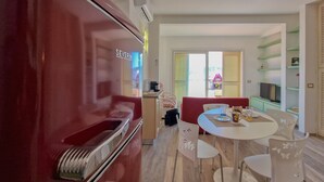 A modern kitchen with a red appliance, a dining area with a white table and chairs, and a view of the outside through large windows. - Apartment 'Terrazza Sul Mare' with Sea View, Wi-Fi and Air Conditioning (Portoferraio)