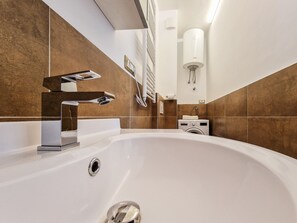 A modern bathroom with a large bathtub, a wall-mounted towel dispenser, and a built-in washing machine.