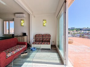 A balcony with a red sofa, a white chair, and a glass table.