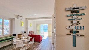 A modern interior with a dining area, a red sofa, and a wall-mounted signpost with directional labels. - Apartment 'Terrazza Sul Mare' with Sea View, Wi-Fi and Air Conditioning (Portoferraio)