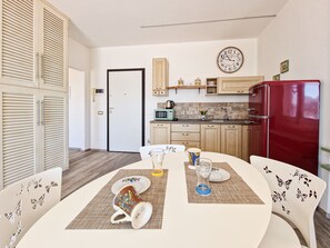A compact kitchen with wooden cabinets, a red refrigerator, a clock, and a dining area with a table set for two.