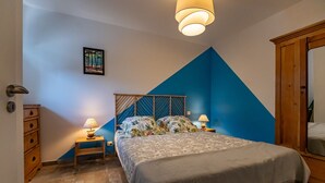 Un dormitorio con cama, dos mesitas de noche con lámparas, un armario de madera, un cuadro en la pared y una pared de acento azul.