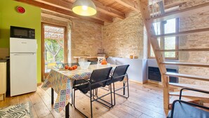 A rustic kitchen with a wooden ceiling, a white refrigerator, a microwave, a table with a colorful tablecloth, and a black chair. - Les Jardins de Boscornut – Organic Farm Cottage near Hautefort in Périgord Noir (Sainte-Orse)