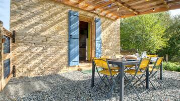 Ein Steinhaus mit einer Holzpergola und einem Tisch mit Stühlen vor der Fassade.