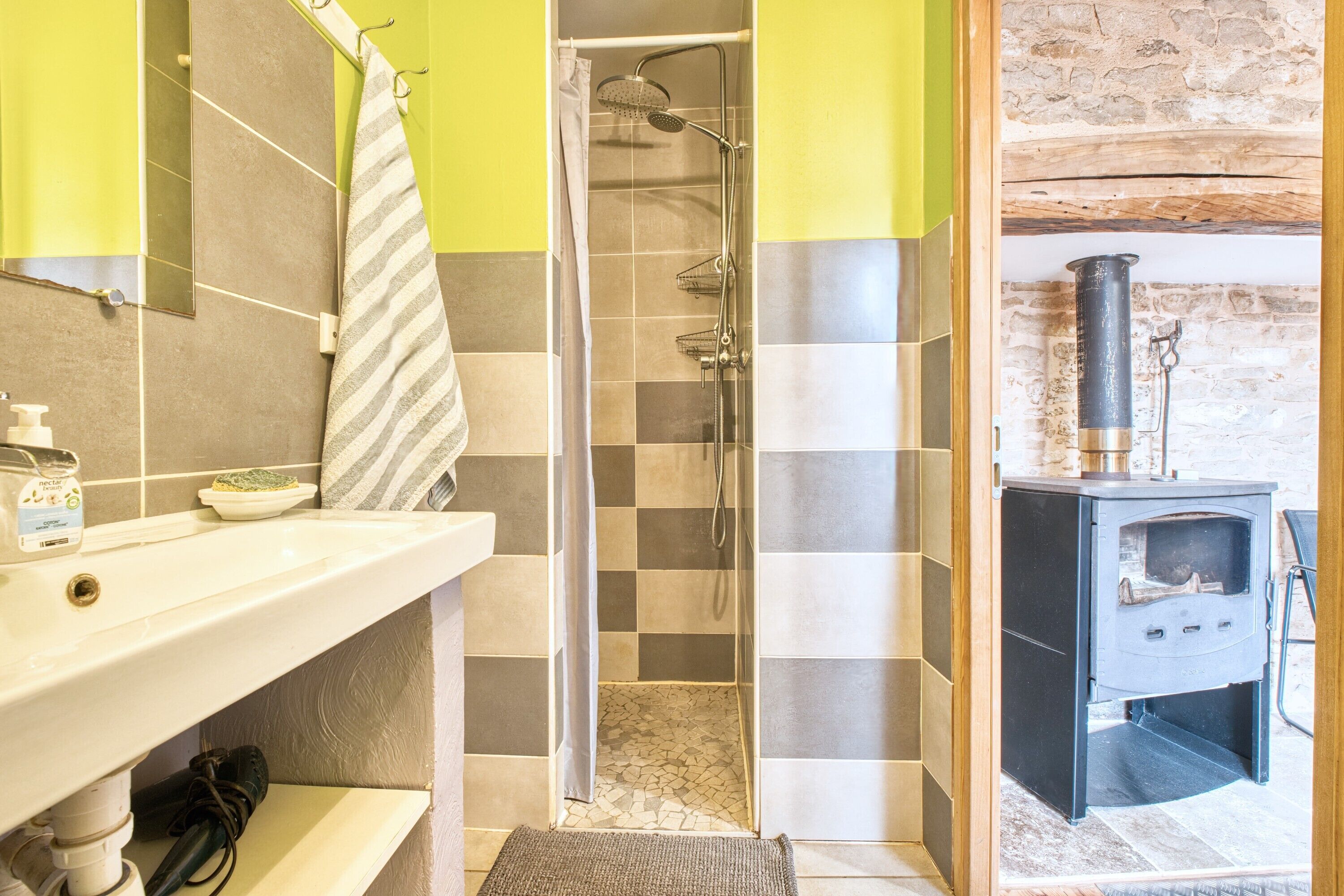 A bathroom with a shower, a sink with toiletries, and a wood-burning stove.