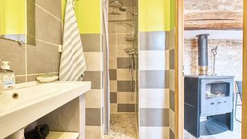A bathroom with a shower, a sink with toiletries, and a wood-burning stove.