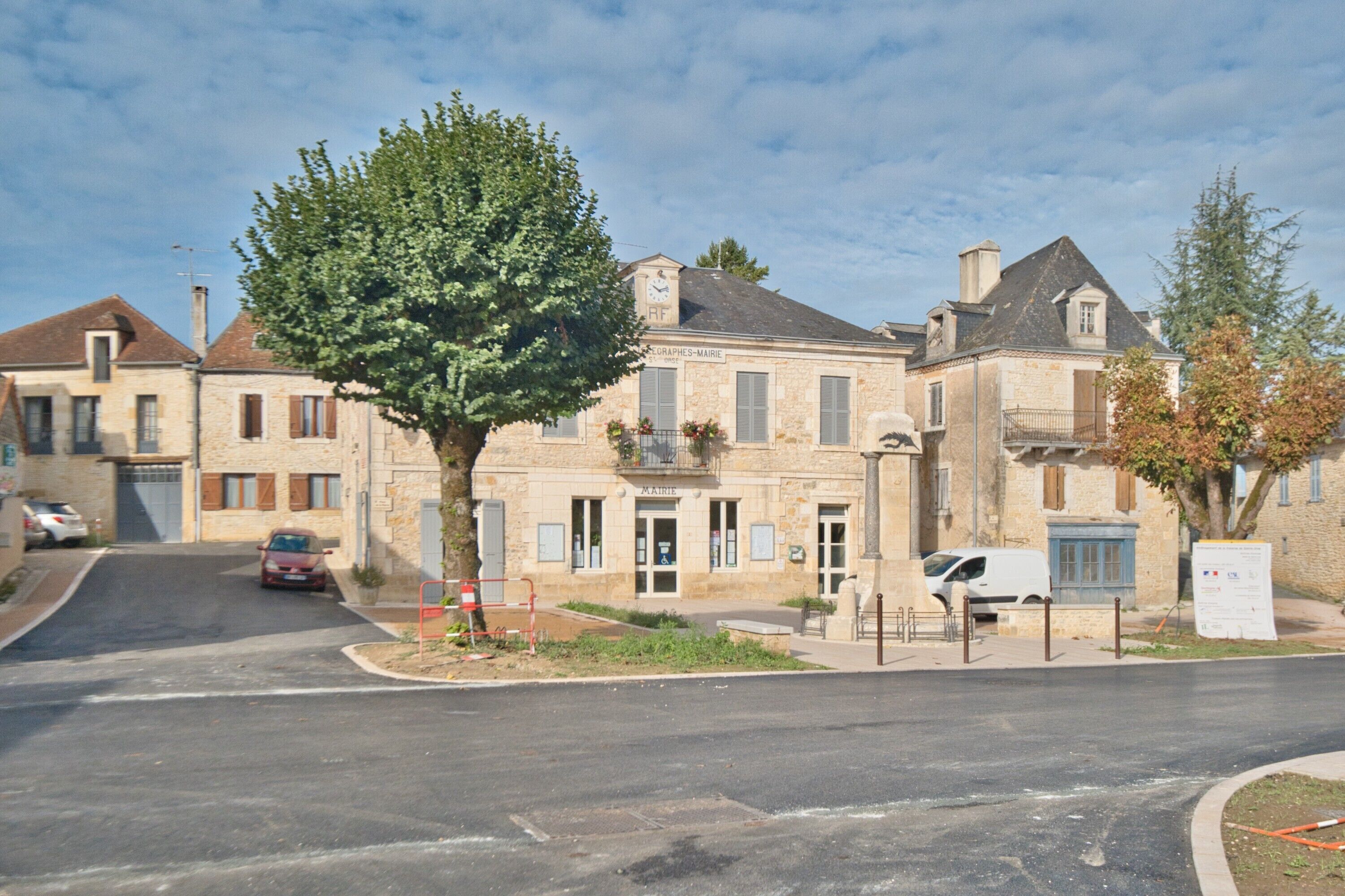 A stone building with a central entrance, a tree in front, and a parked car.