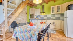 A kitchen with wooden beams, a staircase, and a dining table with a patterned tablecloth. - Les Jardins de Boscornut – Organic Farm Cottage near Hautefort in Périgord Noir (Sainte-Orse)