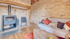 A stone-walled room with a fireplace, a sofa, and a chair. - Les Jardins de Boscornut – Organic Farm Cottage near Hautefort in Périgord Noir (Sainte-Orse)