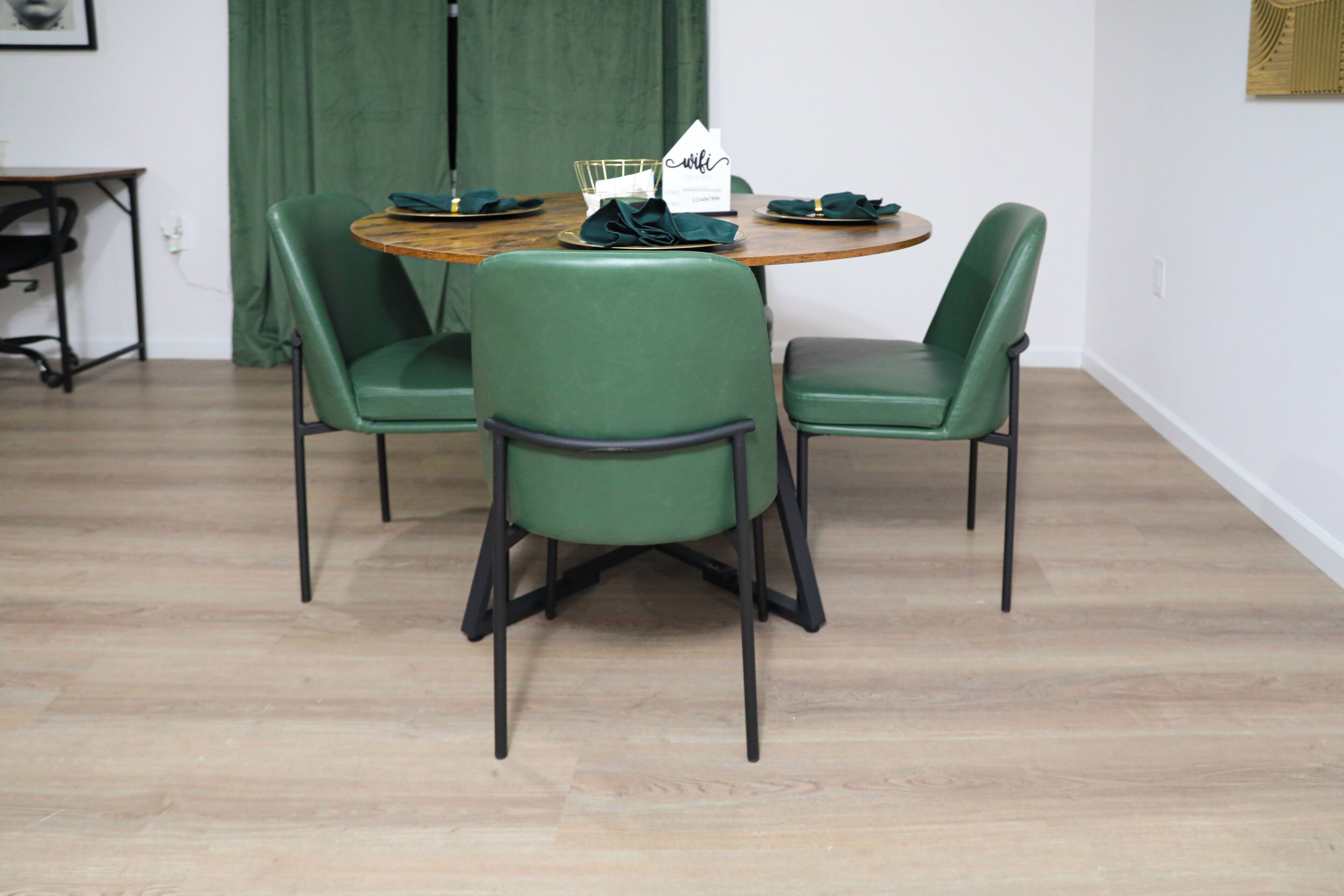 A dining area with a round wooden table, three green chairs, and a green curtain in the background.