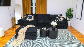 A modern living room with a black sofa, a patterned rug, and a minimalist decor style. - Upscale 3-bedroom/2.5-bath unit near EWR, NYC, MetLife, Prudential, and more. (Newark)