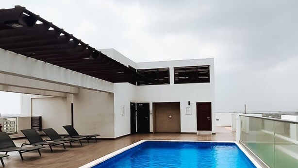 Una piscina interior moderna con un deck de madera, sillas de descanso y una zona cubierta con techo.
