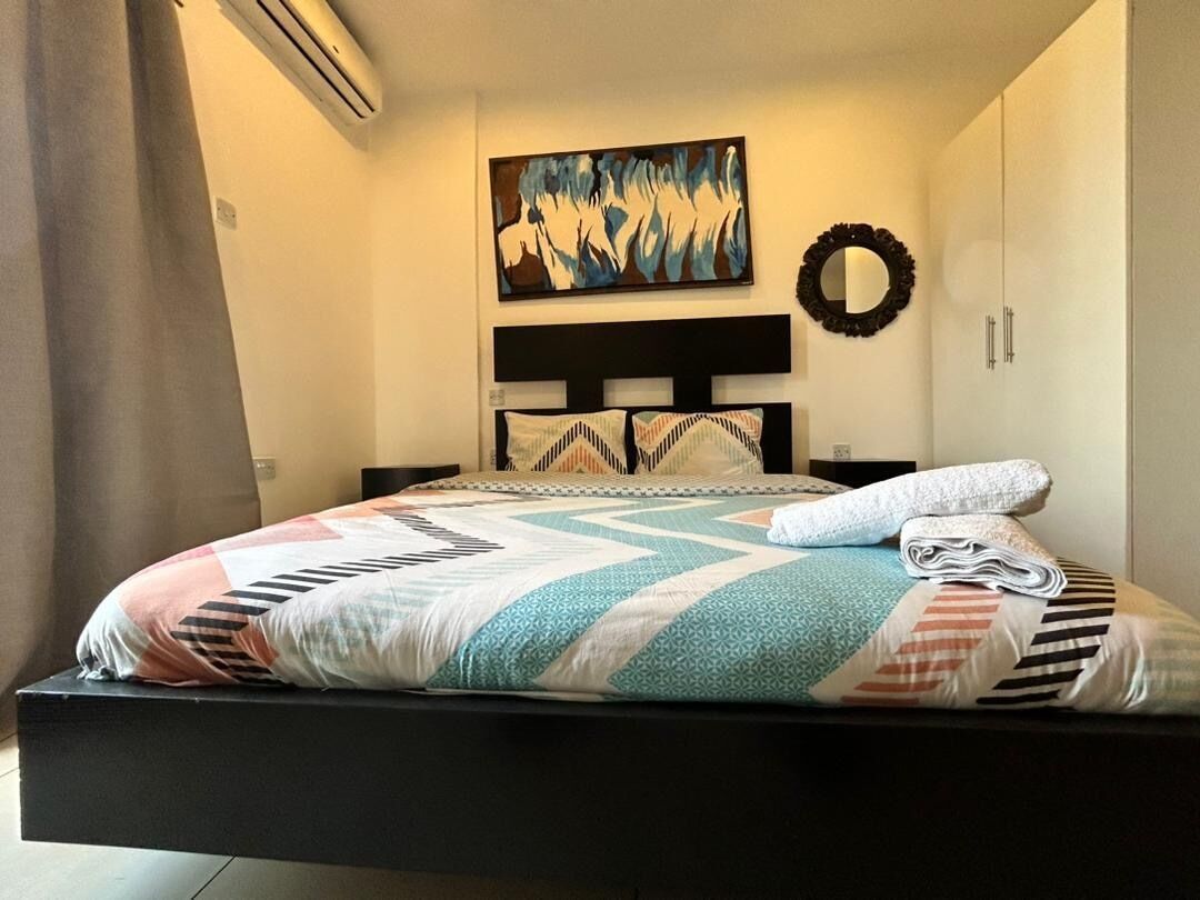 Ein Bett mit Decke, einem Kopfteil, einem Wandbild und einem Spiegel.
