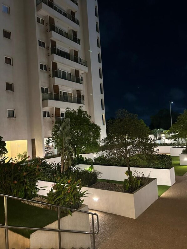 Un bâtiment moderne doté de nombreux balcons et d’un espace extérieur bien éclairé, agrémenté de jardinières et d’un chemin.