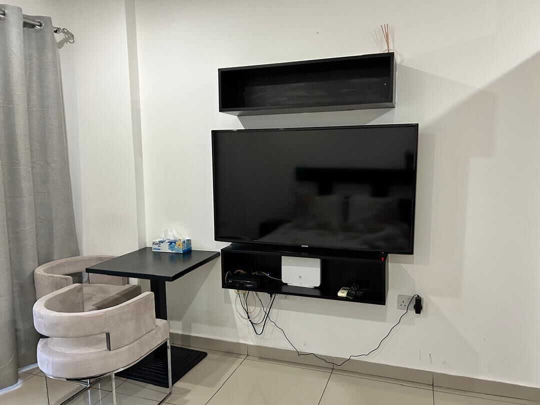 A modern living room with a flat-screen TV mounted on the wall, a small table with a remote control, and a comfortable chair.