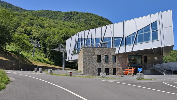 Un edificio moderno con un diseño arquitectónico único, un camino pavimentado en primer plano y montañas al fondo.