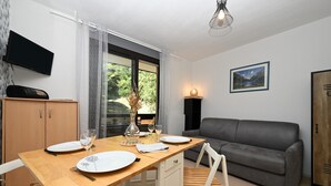 Un comedor con una mesa de madera, sillas blancas, un sofá gris y un televisor fijado a la pared.