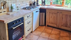 Une cuisine rustique avec des meubles en bois, un four encastré et une vue sur l’extérieur grâce à de grandes fenêtres.