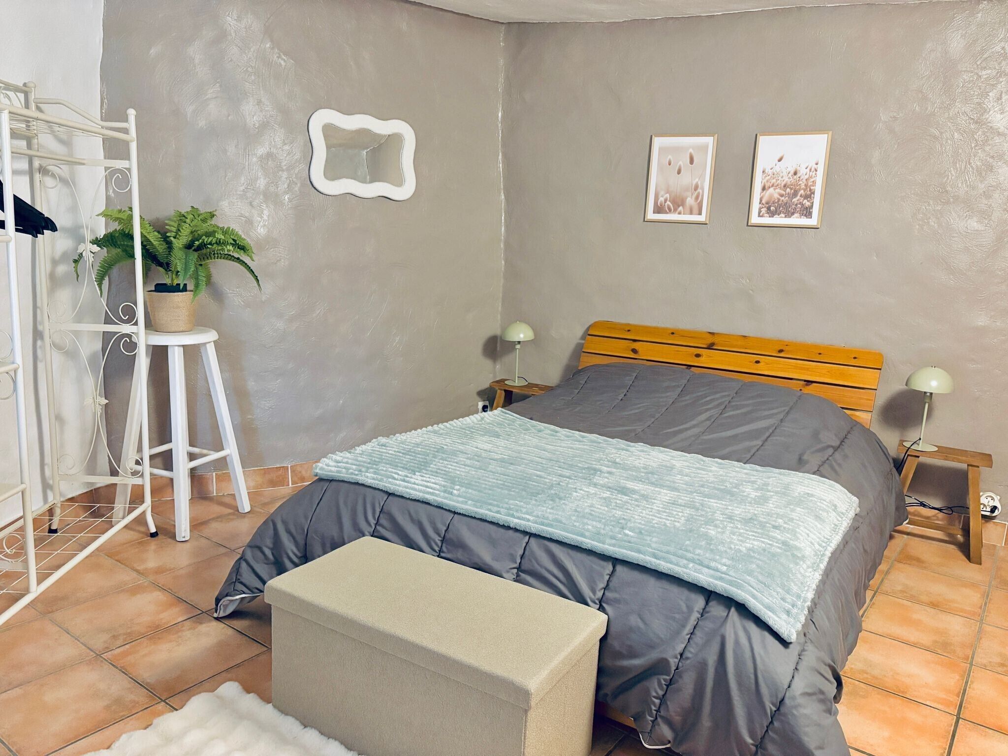 Une chambre à coucher comprenant un lit, une table de chevet, une lampe, une plante en pot, un miroir et une étagère fixée au mur.